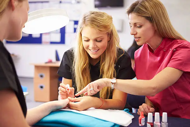 Teacher Helping Students Training To Become Beauticians Painting Nails