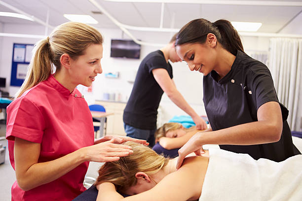 profesor ayudando a estudiantes de capacitación para convertirse en un masajista - massage therapist fotografías e imágenes de stock