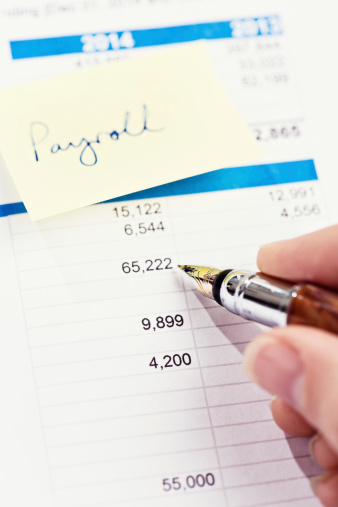 A  fountain pen checks a financial or business document with an adhesive note reading \