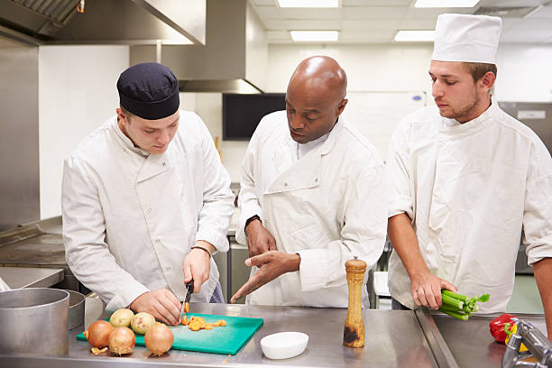 Teacher Helping Students Training To Work In Catering Teacher Helping Students Training To Work In Catering Chopping Vegetables cooking class photos stock pictures, royalty-free photos & images
