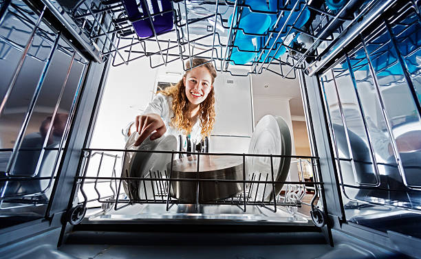 Looking out from dishwasher interior at young woman loading dishes A smiling young woman seen, unusually, from inside the dishwasher drum, loads or unloads dishes. dishwasher stock pictures, royalty-free photos & images