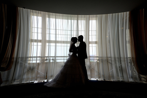 silhouette bride and groom kissing in front of narrow window.