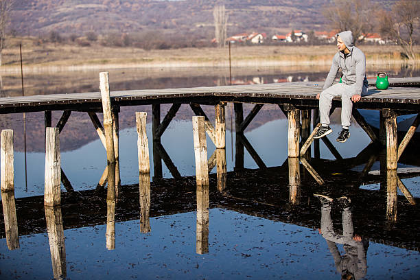 Man with a hood sitting on the pier by the lake