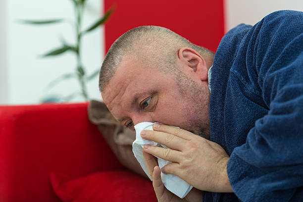 istock Man blowing his nose in his living room 511812082