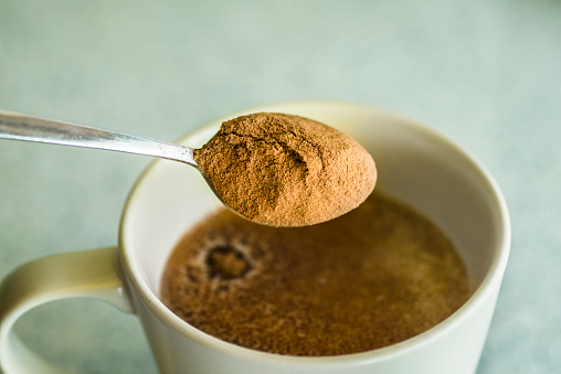 A spoon with powdered cocoa falling on a mug with milk.
