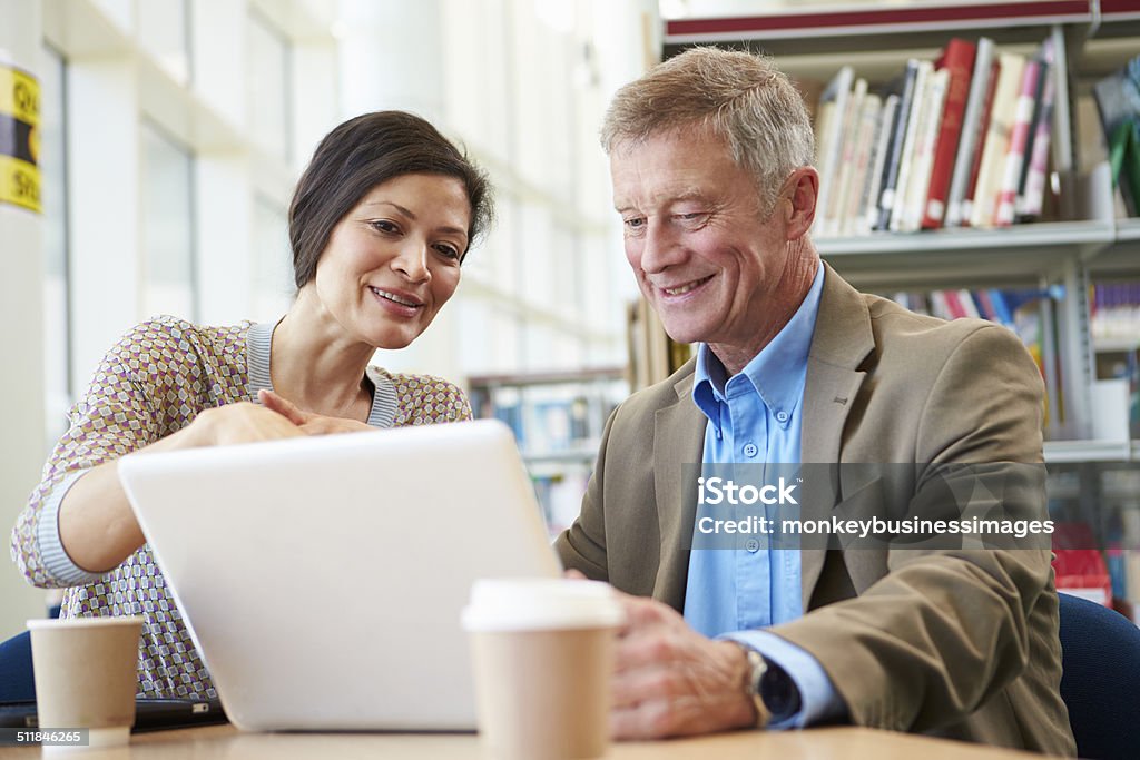 Teacher Helping Mature Student With Studies In Library Teacher Helping Mature Student With Studies In Library Looking At Laptop Professor Stock Photo
