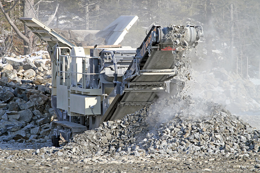 Close up of rock crusher in action, crushing large chunks of rock into smaller pieces which will be used for road bed on a new road construction project. Shallow dof with focus on gravel leaving conveyor belt.