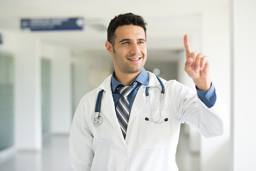 Happy doctor at the hospital pointing something with his finger - healthcare and medicine,