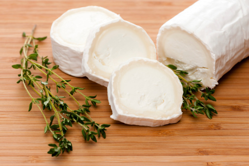 Slices of Goat cheese with fresh thyme on a Bamboo Cutting board.