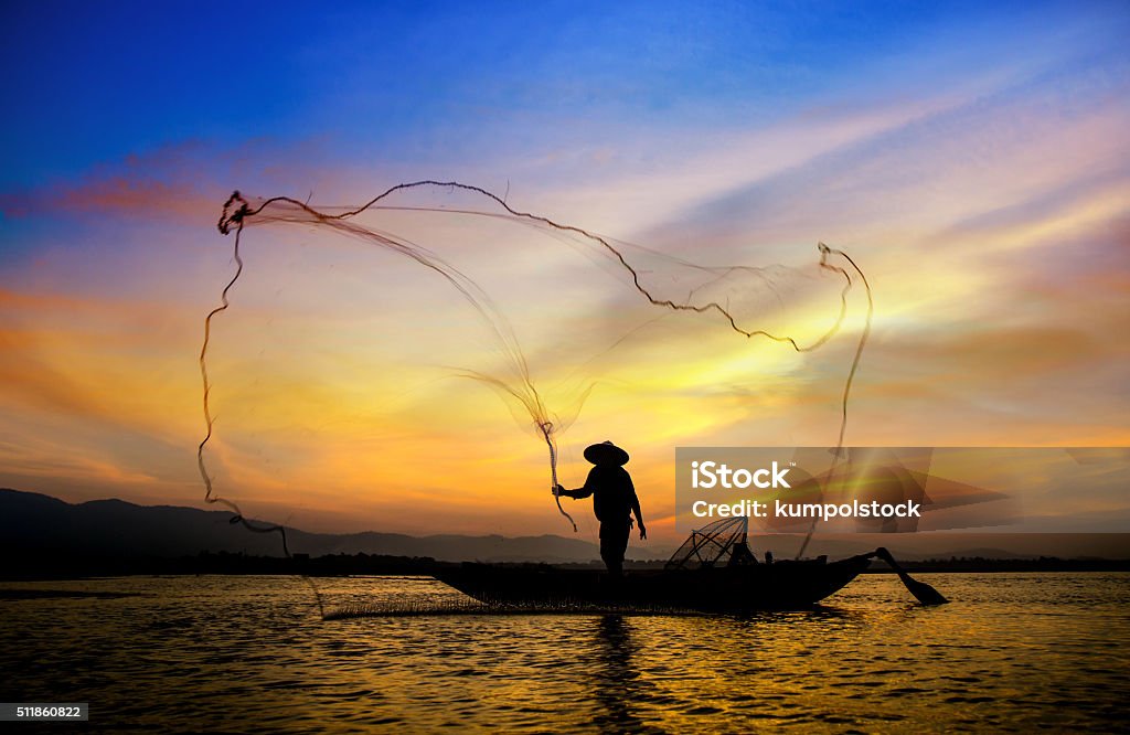 Silhouette of traditional fishermen throwing net fishing. Silhouette of traditional fishermen throwing net fishing lake at sunrise time. Thailand.(The casting people living along the River) Activity Stock Photo