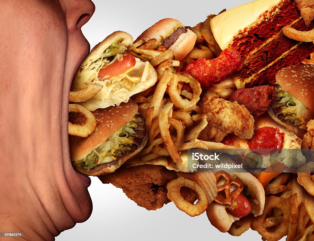 Eating Junk Food Eating junk food nutrition and dietary health problem concept as a person with a big wide open mouth feasting on an excessive huge group of unhealthy fast food and snacks. Over Eating Stock Photo