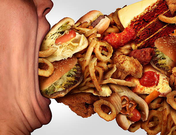 Eating Junk Food Eating junk food nutrition and dietary health problem concept as a person with a big wide open mouth feasting on an excessive huge group of unhealthy fast food and snacks. greed stock pictures, royalty-free photos & images