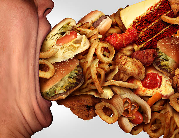 Eating Junk Food Eating junk food nutrition and dietary health problem concept as a person with a big wide open mouth feasting on an excessive huge group of unhealthy fast food and snacks. over eating stock pictures, royalty-free photos & images