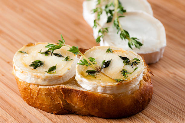 Goat cheese with thyme and gratinated with honey Goat cheese with fresh thyme and gratinated with honey on a slice of bread. Displayed on a cutting board of bamboo. goat-cheese stock pictures, royalty-free photos & images
