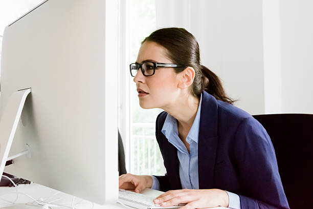 What's that? Confused Business Woman Confused young businesswoman can`t believe what she is reading on her computer screen. Sitting close to the screen trying to understand. Natural Office interior light. mesmerised stock pictures, royalty-free photos & images