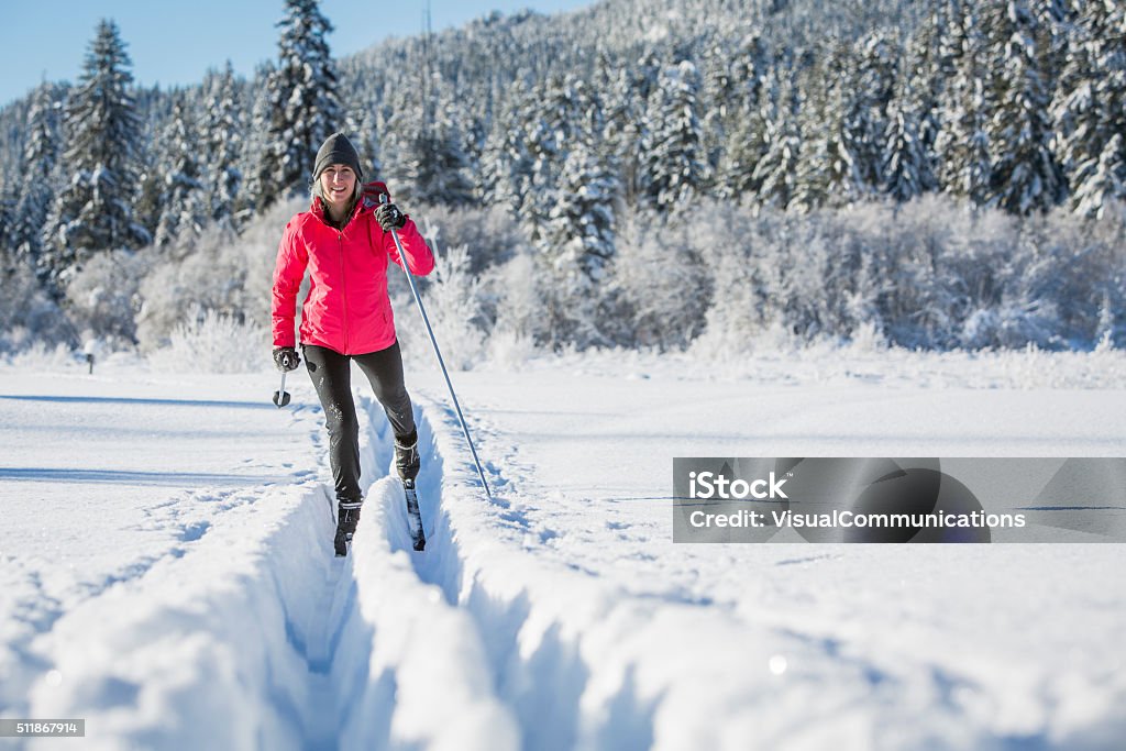 Woman cross country skiing on sunny day. Attractive young woman cross country skiing through deep powder with snowy trees and blu sky in background. Cross-Country Skiing Stock Photo