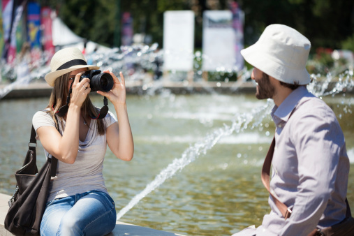 Woman taking a picture of her boyfriend while sitting next to a fountain