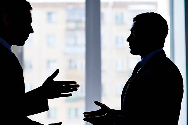 Business dispute Back lit image of two businessmen arguing confrontation stock pictures, royalty-free photos & images