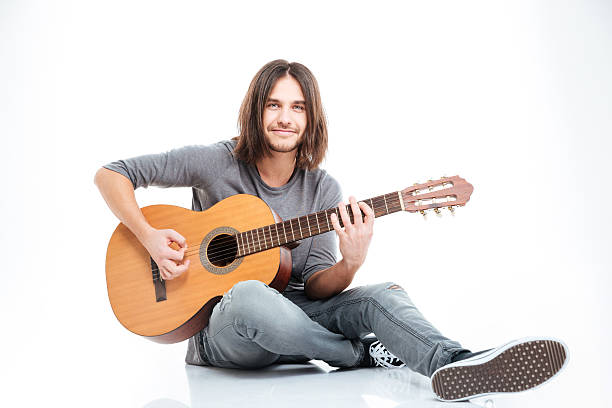 istock Smiling young man sitting on the floor and playing guitar 511869594