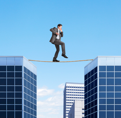 A businessman walking on a tightrope between two buildings.