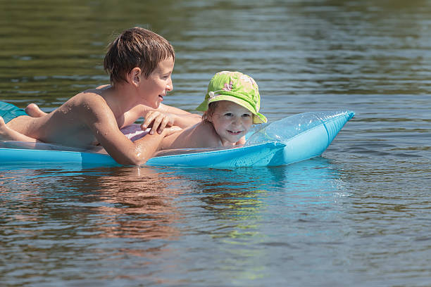 hermanos flotando en colchón inflable en el verano de la piscina al aire libre y estanque - child inflatable raft lake family fotografías e imágenes de stock