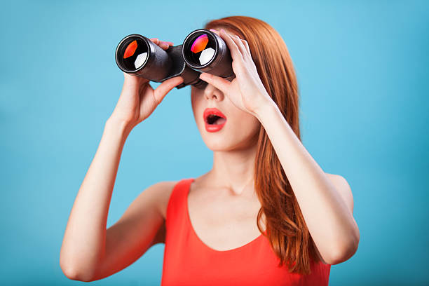 Redhead girl with binocular on blue background.
