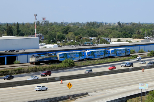 Fort Lauderdale, Florida, USA - March 30, 2013: Tri-Rail engine and three passenger trains moving south next to I-95 Highway. This public transportation links three counties from Mangonia Park to Miami.