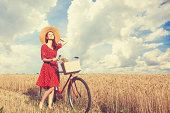 Redhead peasant girl with bicycle on wheat field.