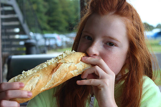 Image of girl eating cheese and pickle sandwich / baguette, cheese-sub