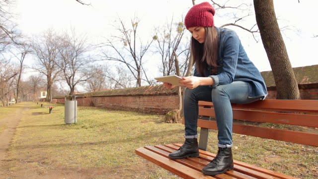 Young rebel woman in park using a digital tablet.