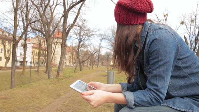 Woman with hat in the park using a digital tablet.
