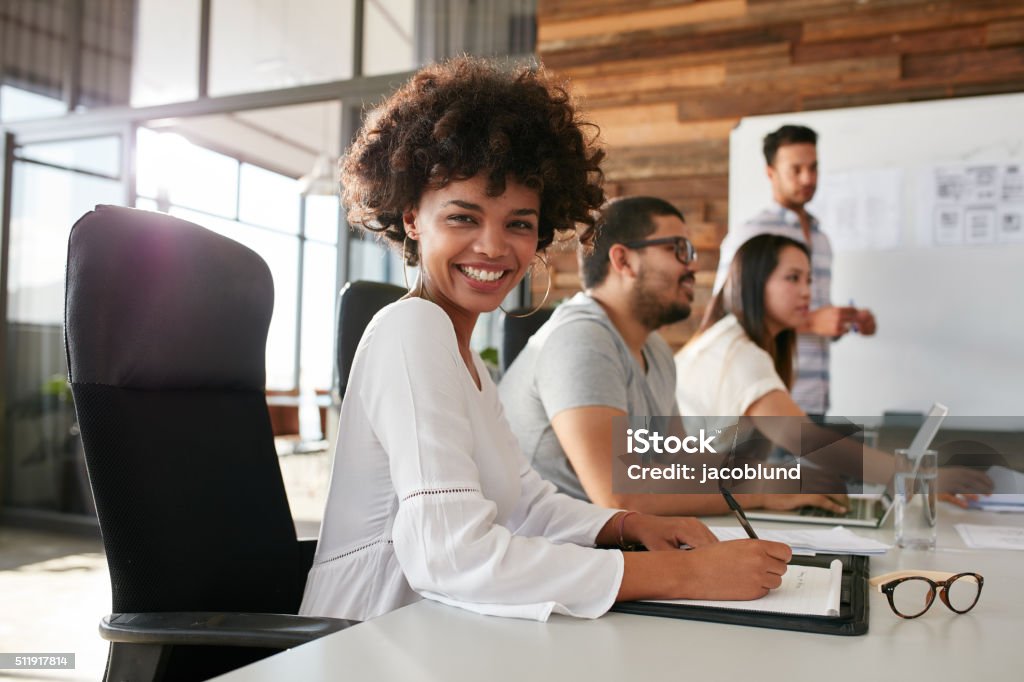 Young african woman sitting at a business presentation Portrait of happy young african woman sitting at a business presentation with colleagues in boardroom. Female designer with coworkers in conference room. Business Stock Photo