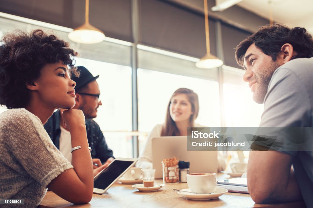 Group of people at coffee shop for startup meeting Portrait of group of young people sitting at a cafe and discussing work. Young men and women at coffee shop for startup meeting. Coffee - Drink Stock Photo