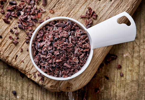 Cacao nibs on wooden table Measuring spoon of cacao nibs on wooden table; top view cacao nib stock pictures, royalty-free photos & images