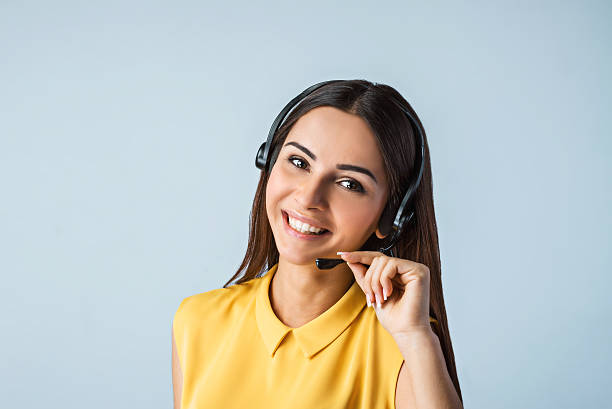 Nice photo of call center operator Photo of beautiful young call center operator standing near gray background. Woman with headphones looking at camera and smiling call center stock pictures, royalty-free photos & images
