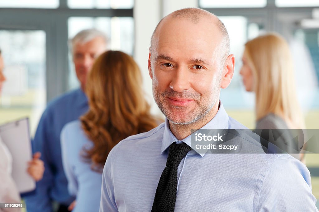 Businessman portrait Close-up portrait of senior businessman standing at business meeting while looking at camera and smiling. Business people standing in background. Bank Teller Stock Photo