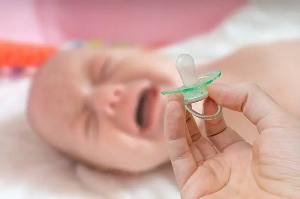 Pacifier in hand and crying baby in background.
