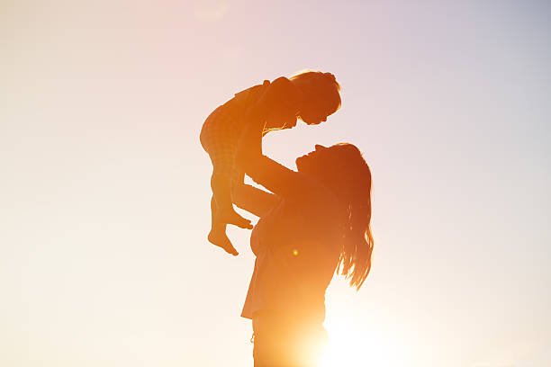 mother and little daughter play at sunset sky