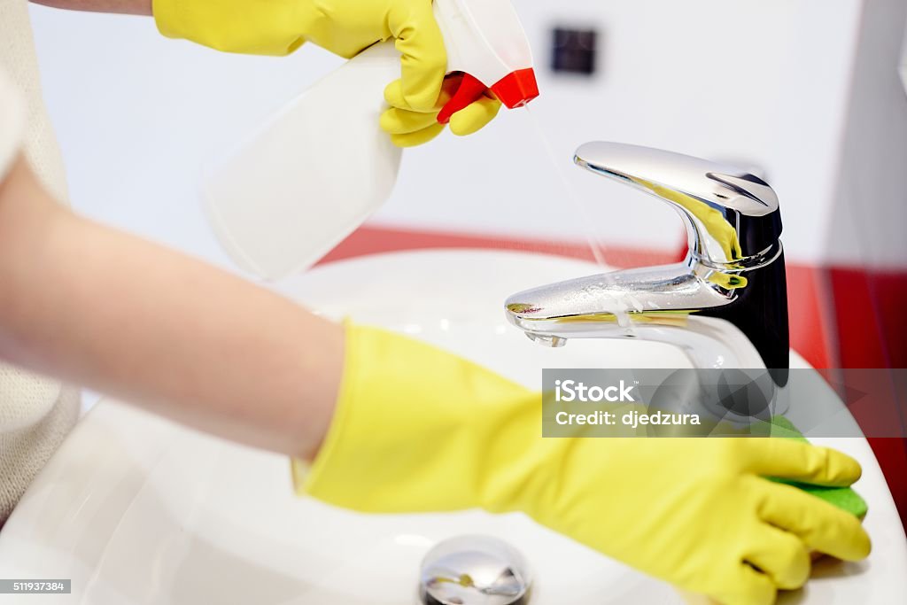 Female hands  spraying liquid detergent on tap Female hands with rubber gloves spraying liquid detergent on tap and cleaning it with sponge. Spring cleaning Adult Stock Photo