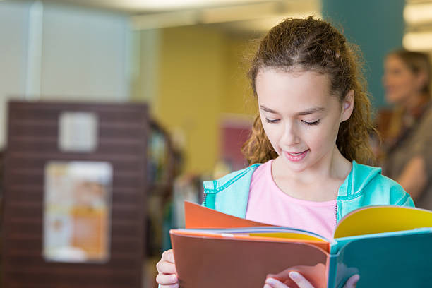 istock Elementary age girl reading childrens book in public library 511941052