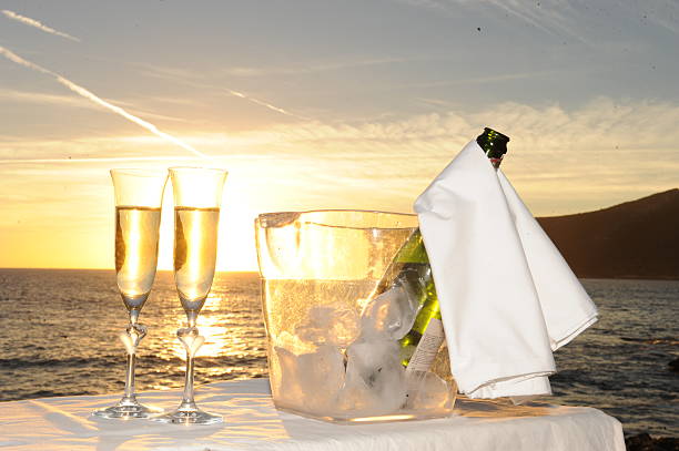 Close-up of female tattooed hand holding sparkling wine glass at outdoors summer party at sunset