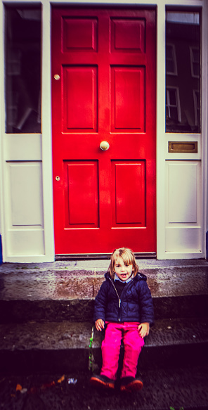 Little girl sits on the front step, behind her, a vibrantly painted red door