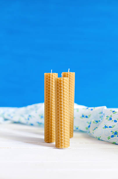 Three candles made from natural wax by hand on a light blue background. The decor of soft tissue in the rustic style
