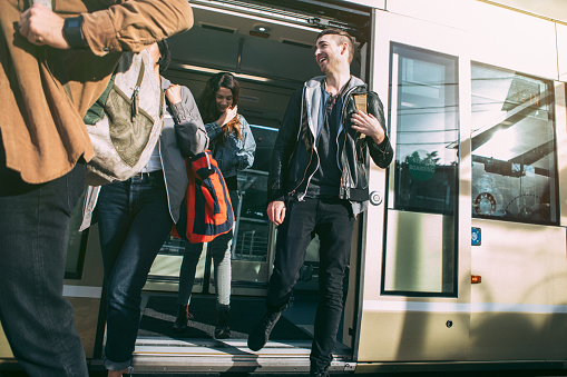 A group of young adult friends exit from the new street car in Capitol Hill, Seattle, Washington.  Bright sunlight illuminates the scene.  Horizontal image.