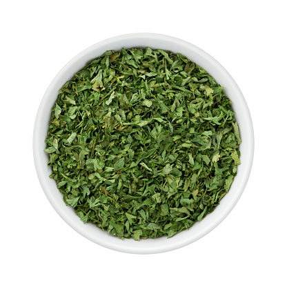 Dried Parsley Flakes in a Ceramic Bowl. The image is a cut out, isolated on a white background, with a clipping path.