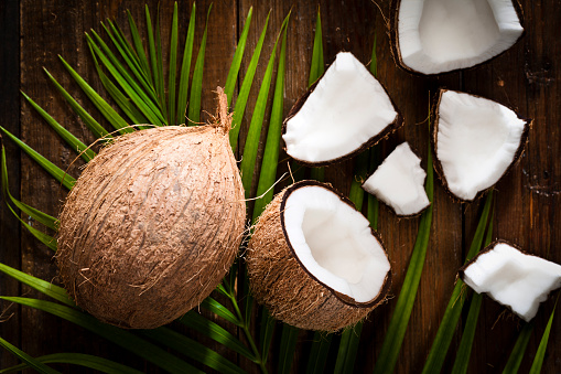 Two whole coconuts, open coconut and coconut pieces shot on rustic wood table. DSRL studio photo taken with Canon EOS 5D Mk II and Canon EF 100mm f/2.8L Macro IS USM