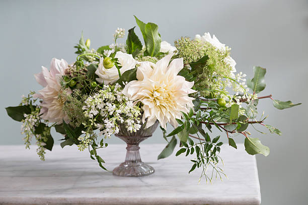 Bouquet of Flowers An elaborate bouquet of flowers in  a vase.  All the flowers are white with some greenery mixed in.  The vase sits on a marble surface and in front of a blank gray background.  The lighting is natural and soft.  Nobody is in the photograph. flower arrangement stock pictures, royalty-free photos & images
