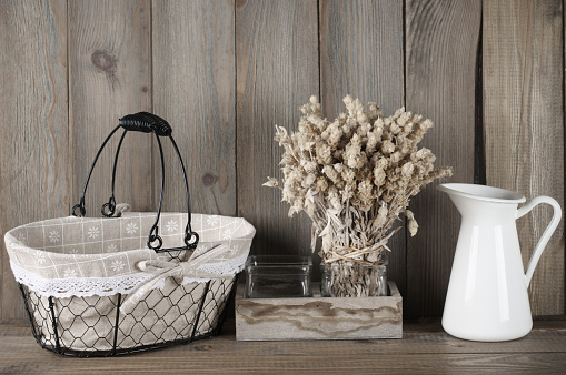 Rustic kitchen still life: dried flowers bunch, wire basket and jug against vintage wooden background.