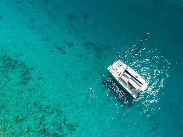Aerial view of people snorkeling and relaxing on catamaran anchored in clear tropical water in the Caribbean