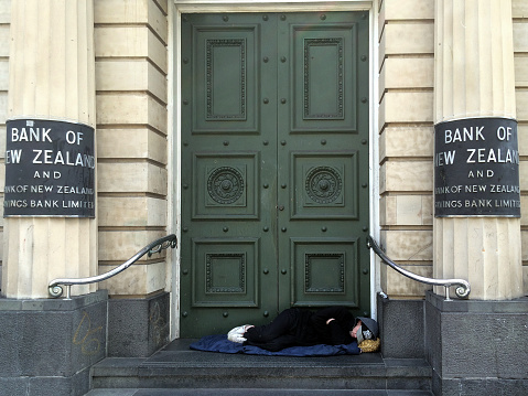 Auckland, New Zealand - October 5, 2015: A homeless sleeps under the doorway of New Zealand Bank in Auckland. In 2104 Statistics New Zealand estimated about one in 120 New Zealanders were homeless or housing